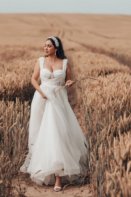 Robe de mariée blanche longue et charmante, coupe trapèze, sans manches, en tulle et dentelle.