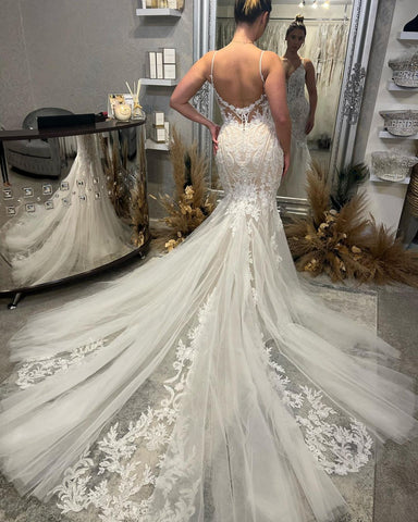 Elegante vestido de novia de corte sirena, sin mangas, con escote en V, tirantes finos y largo hasta el suelo, con cola de capilla.