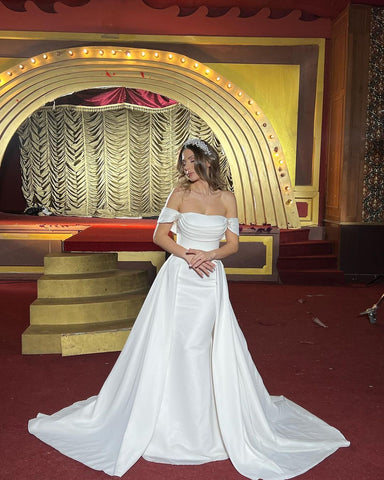 Robe de mariée longue chic de coupe trapèze, épaules dénudées, sans manches et avec traîne amovible.