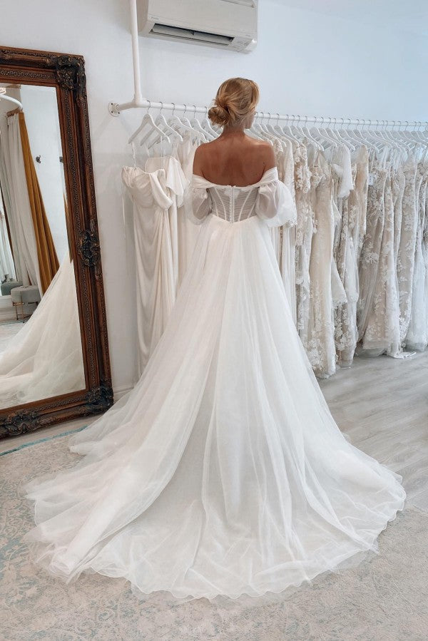 Robe de mariée chic en tulle, manches longues, coupe trapèze, décolleté cœur et fente sur le devant, avec traîne chapelle.