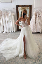 Robe de mariée chic en tulle, manches longues, coupe trapèze, décolleté cœur et fente sur le devant, avec traîne chapelle.