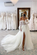 Robe de mariée chic en tulle, manches longues, coupe trapèze, décolleté cœur et fente sur le devant, avec traîne chapelle.