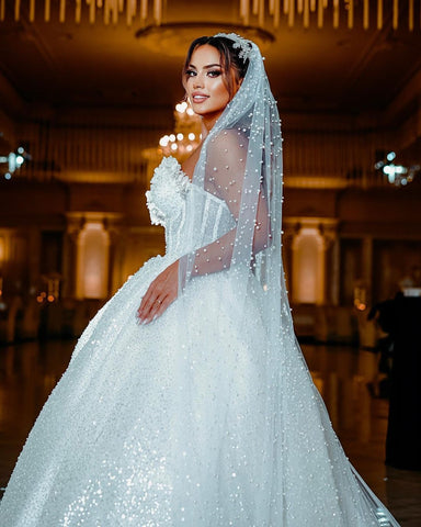 Robe de mariée de luxe longue au sol, décolleté cœur sans manches, coupe trapèze, ornée de sequins et de perles.