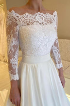 Robe de mariée blanche en satin et dentelle, coupe trapèze, manches longues, ornée d'appliqués