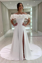 Robe de mariée blanche en satin, coupe trapèze, épaules dénudées, sans manches et fendue.