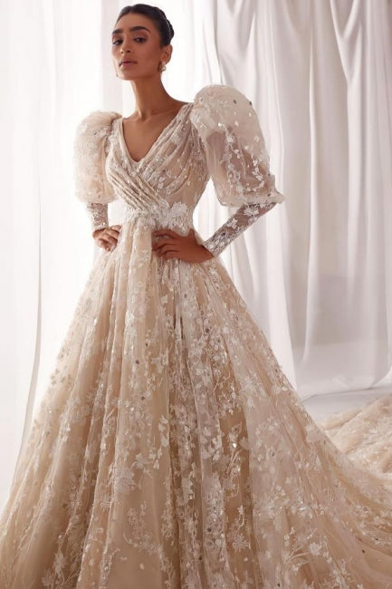 Robe de mariée trapèze en tulle et dentelle, col en V, manches longues, ornée d'appliqués et de volants.
