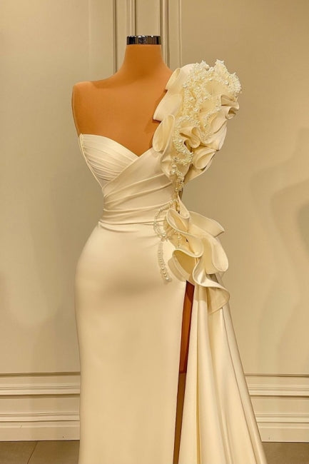 Robe de mariée longue blanche asymétrique à volants et paillettes, ornée d'une épaule dénudée et fendue.