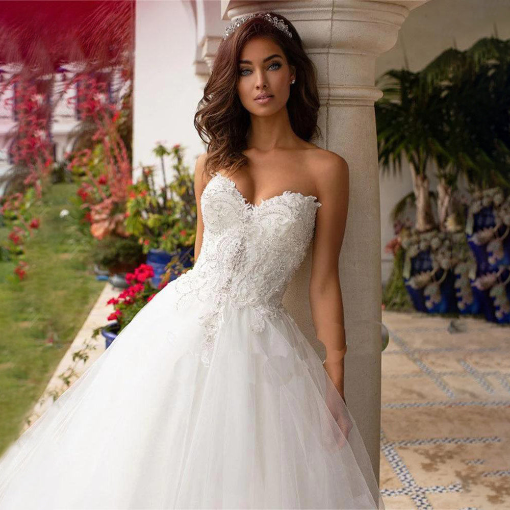Vestido de novia de lujo estilo princesa, con espalda descubierta, corpiño de lentejuelas y pedrería, escote corazón, apliques de encaje y falda de organza con volumen. 
