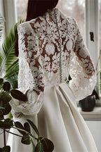Robe de mariée élégante en satin et dentelle, coupe trapèze, col montant, manches longues et poches.