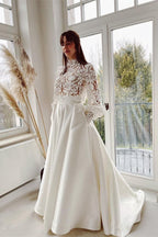 Robe de mariée élégante en satin et dentelle, coupe trapèze, col montant, manches longues et poches.