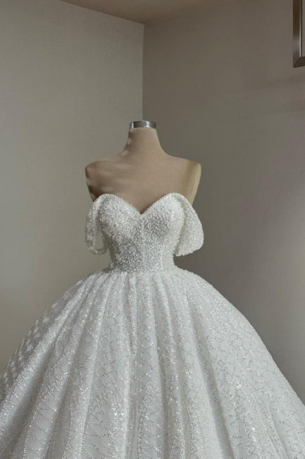 Robe de mariée extravagante blanche longue en dentelle, coupe trapèze, épaules dénudées, ornée de perles