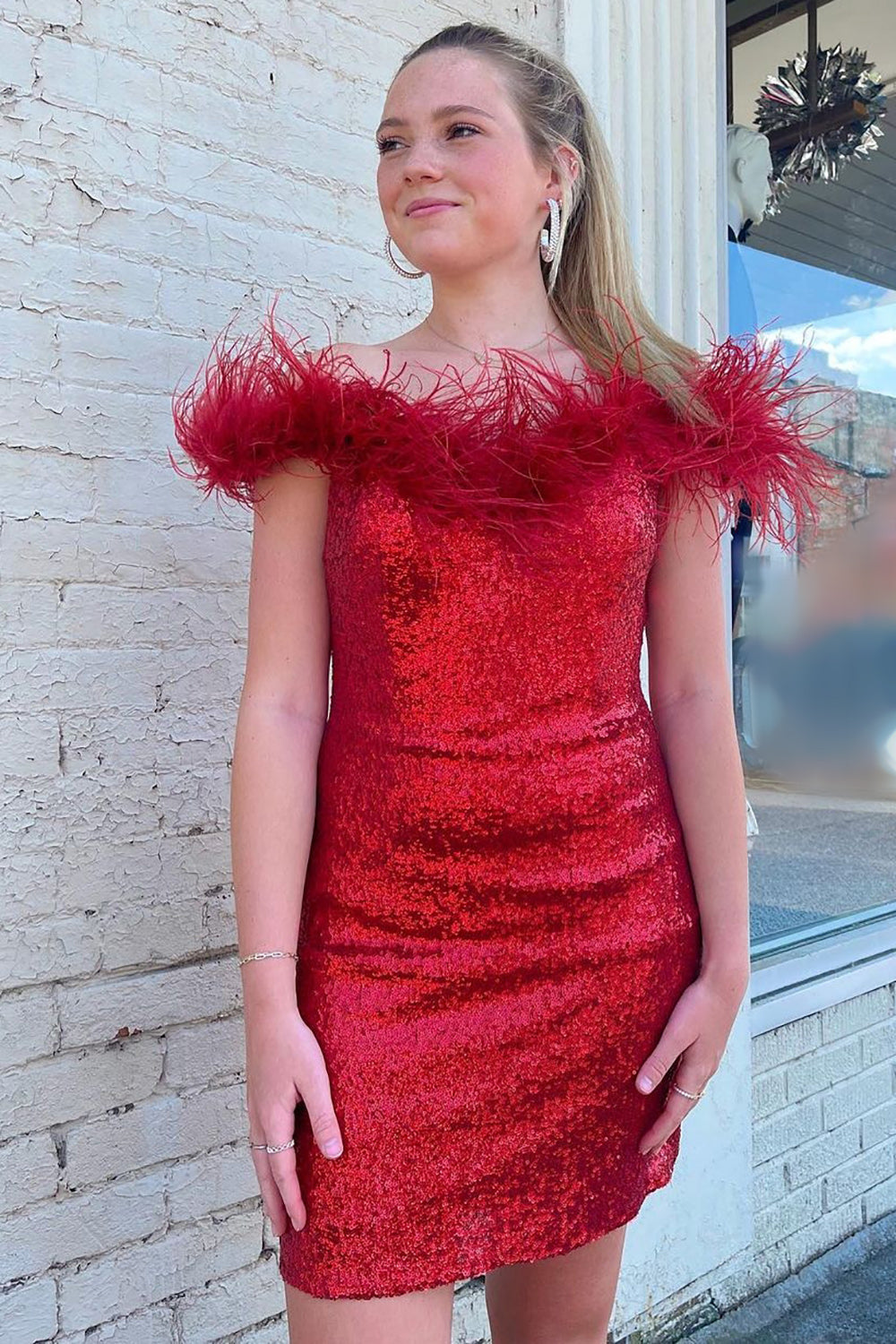 Vestido corto rojo brillante de corte sirena con hombros descubiertos y detalles de plumas para baile de bienvenida.