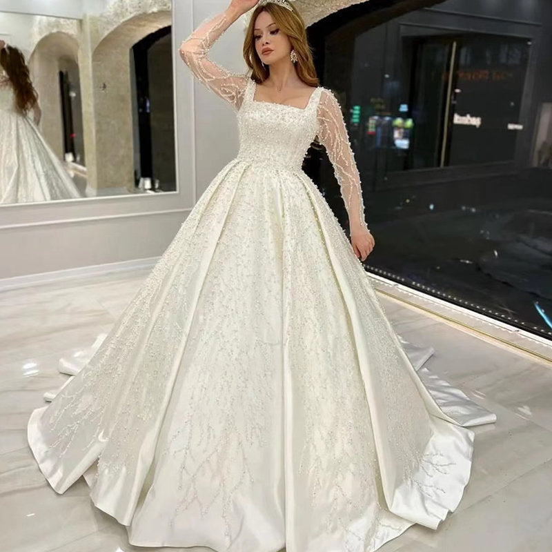 Vestido de novia de lujo con encaje bordado y pedrería, corte princesa, cuello cuadrado, manga larga y botones. 