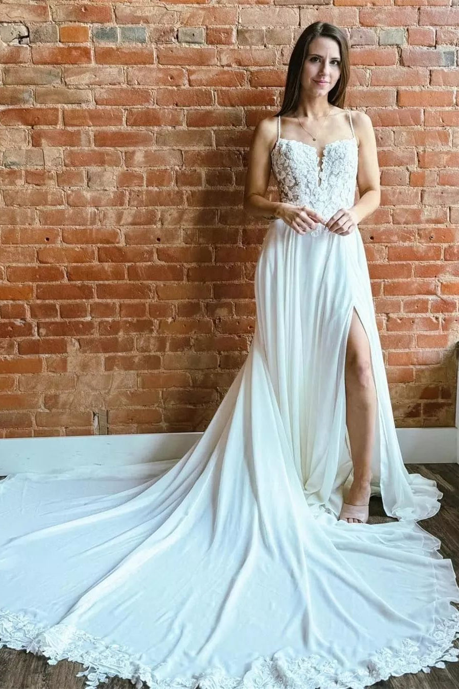 Magnifique robe de mariée blanche sans manches, coupe trapèze, bretelles spaghetti en dentelle et traîne fendue.