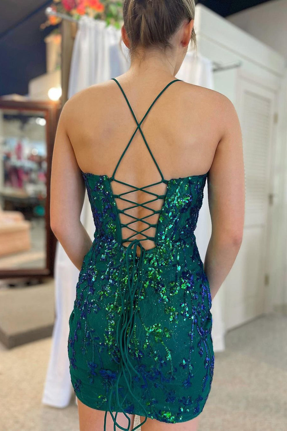 Vestido corto verde oscuro brillante de corte sirena con hombros descubiertos y detalles de plumas.