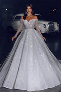 Robe de mariée glamour en dentelle, coupe trapèze, épaules dénudées, manches longues et traîne