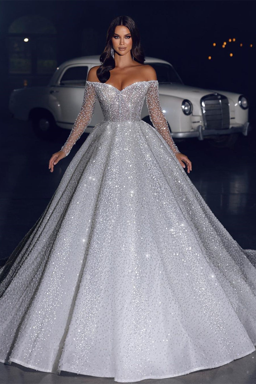 Robe de mariée glamour en dentelle, coupe trapèze, épaules dénudées, manches longues et traîne