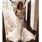 Vestido de novia sirena glamuroso con hombros descubiertos, mangas largas, escote en V y apliques.