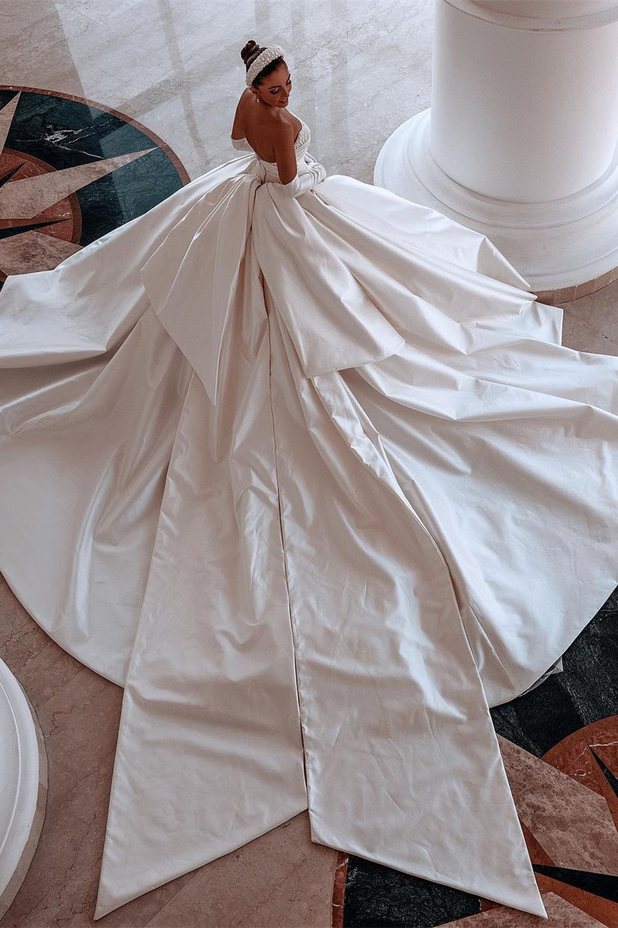 Robe de mariée glamour en satin blanc, coupe trapèze, ornée de perles et avec traîne