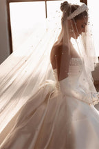 Robe de mariée glamour en satin blanc, coupe trapèze, ornée de perles et avec traîne