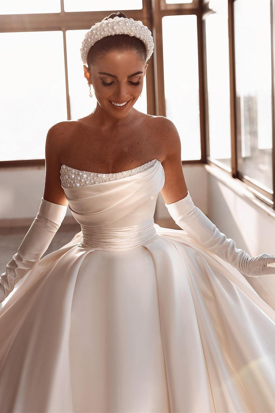 Robe de mariée glamour en satin blanc, coupe trapèze, ornée de perles et avec traîne