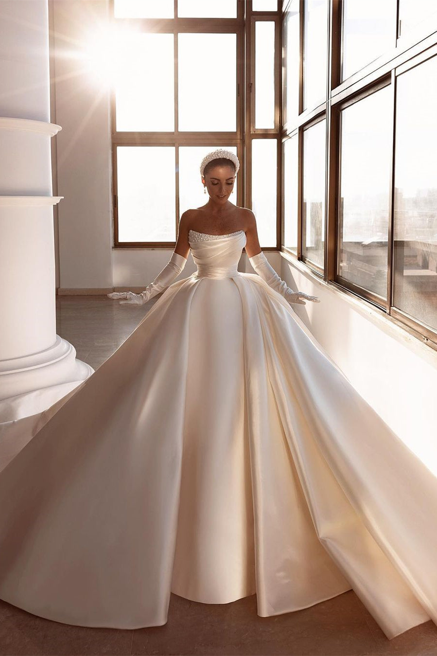 Robe de mariée glamour en satin blanc, coupe trapèze, ornée de perles et avec traîne
