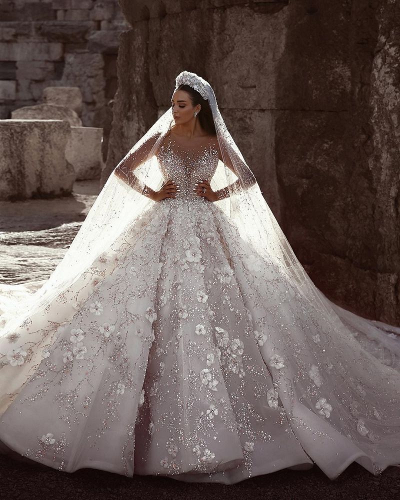 Magnifique robe de mariée princesse à manches longues et col transparent, ornée de perles et de fleurs.