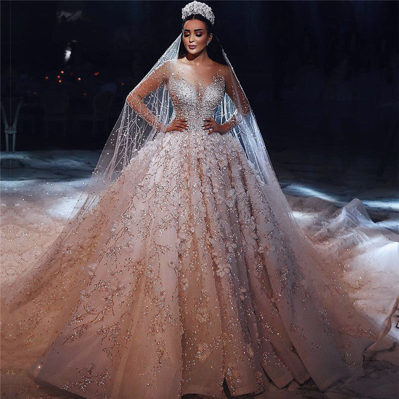 Magnifique robe de mariée princesse à manches longues et col transparent, ornée de perles et de fleurs.