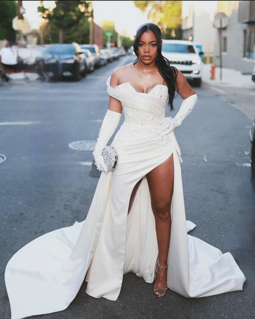 Precioso vestido de novia blanco de corte columna, de satén, sin mangas, con un solo hombro y cola con abertura y detalles de pedrería.