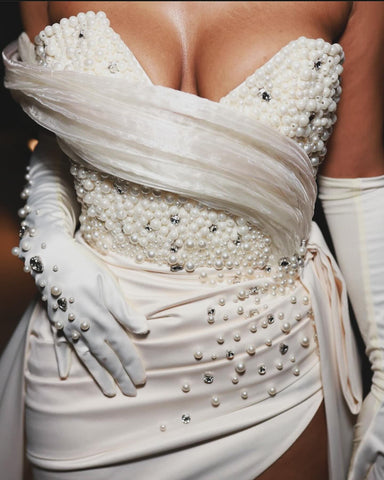 Precioso vestido de novia blanco de corte columna, de satén, sin mangas, con un solo hombro y cola con abertura y detalles de pedrería.