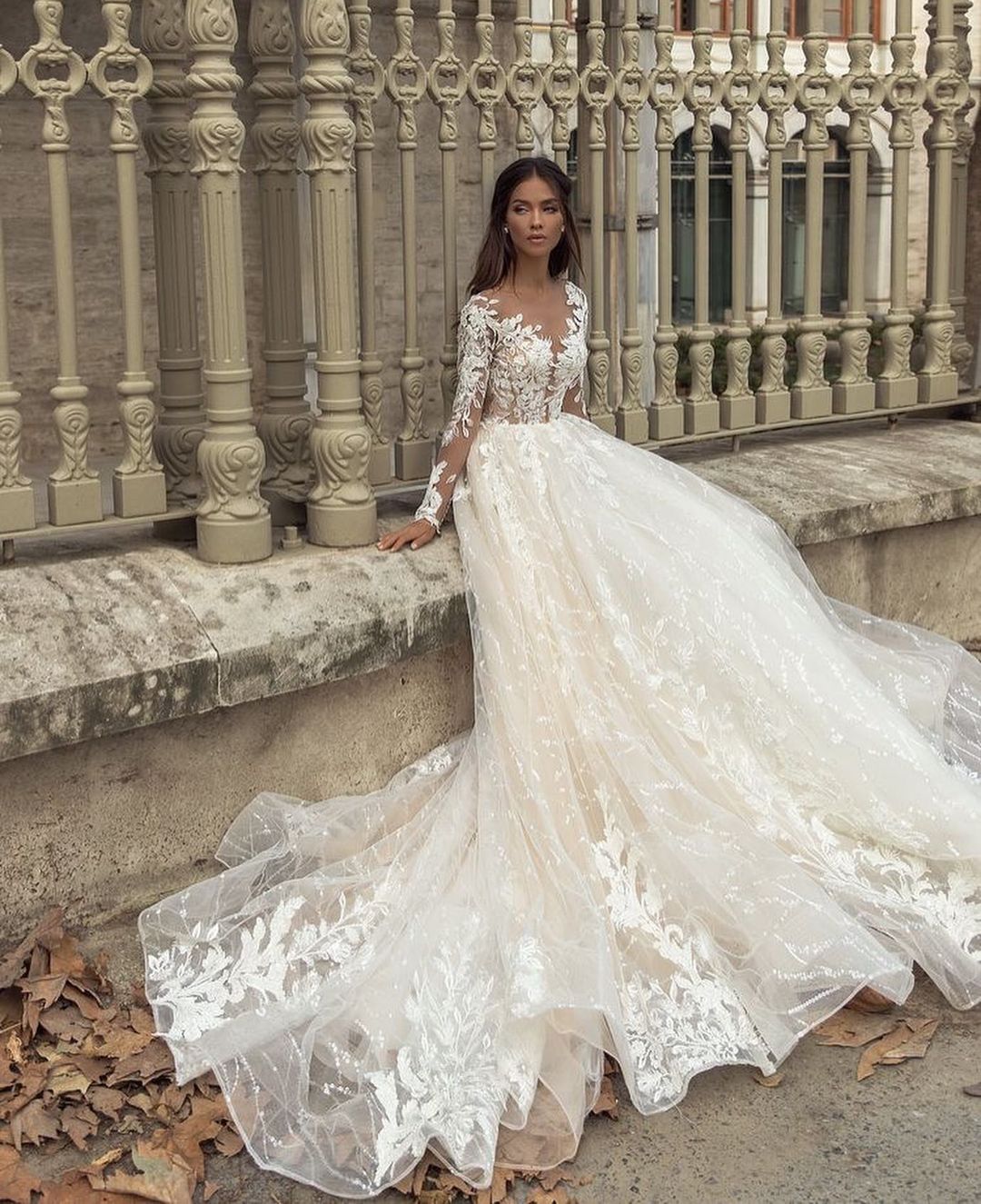 Precioso vestido de novia largo de corte A con escote barco, apliques, cola de encaje y mangas, con mangas y apliques.