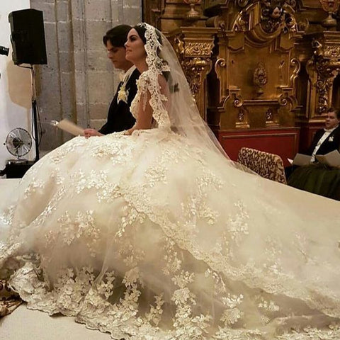 Precioso vestido de novia largo estilo princesa con escote barco, apliques de encaje, espalda descubierta, volantes y mangas.