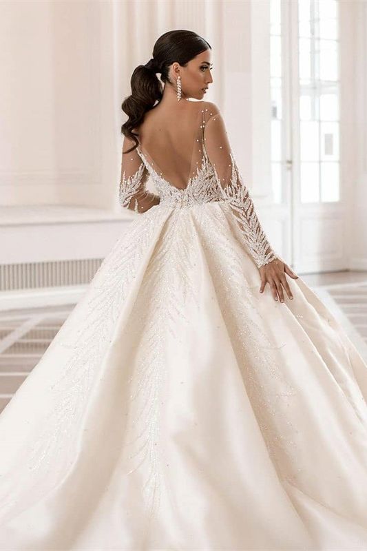 Magnifique robe de mariée en satin ornée de cristaux et de perles, à manches longues et coupe trapèze, ornée de manches longues et d'une coupe bateau.