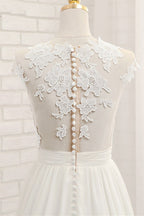Robe de mariée longue en mousseline de soie ornée d'appliqués de dentelle et fendue, coupe trapèze.