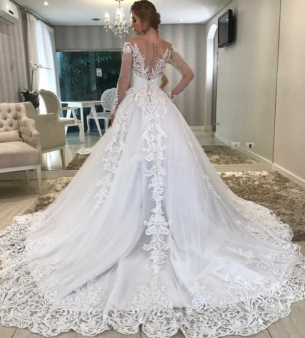 Robe de mariée longue trapèze à décolleté cœur, épaules dénudées, ornée d'appliqués de dentelle et de sequins, avec manches