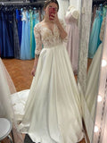 Robe de mariée longue en satin et dentelle, coupe trapèze, décolleté cœur, manches, couleur ivoire.