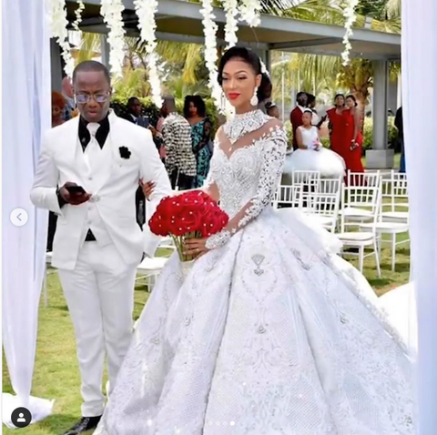 Vestido de novia largo de corte princesa, cuello alto, apliques brillantes, satén y mangas largas.