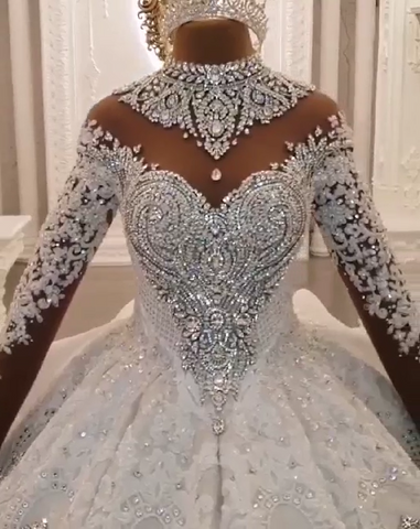 Vestido de novia largo de corte princesa, cuello alto, apliques brillantes, satén y mangas largas.