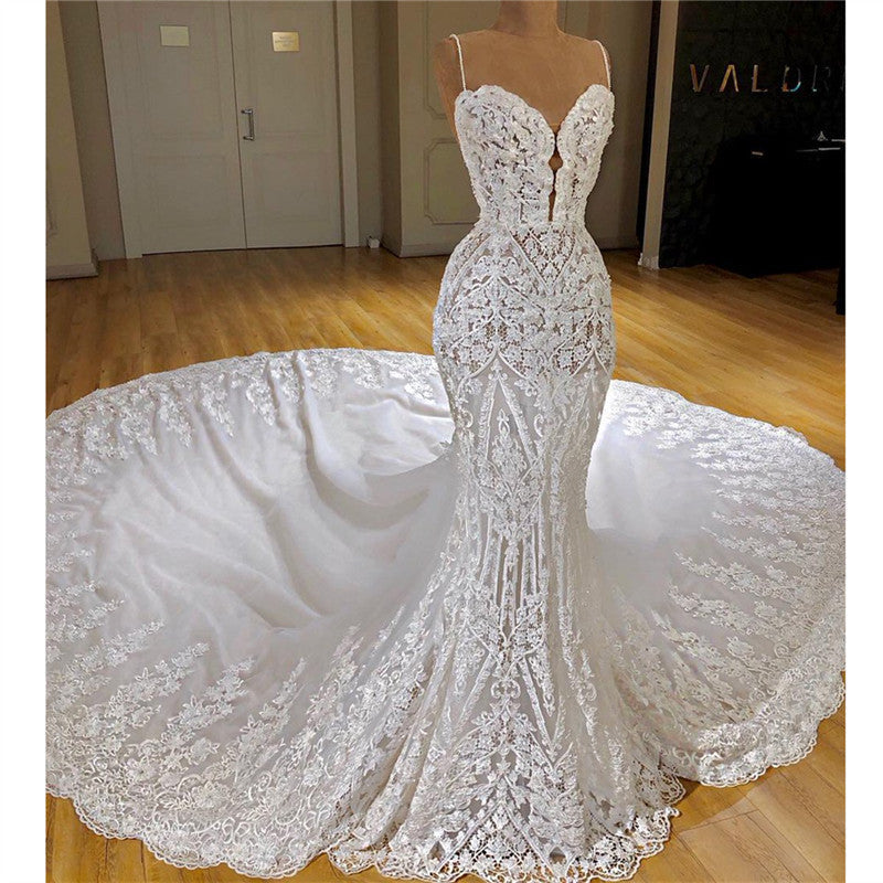 Robe de mariée sirène longue à fines bretelles spaghetti, ornée d'appliqués de dentelle et d'une traîne cathédrale.