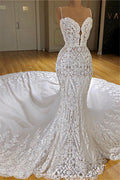 Robe de mariée sirène longue à fines bretelles spaghetti, ornée d'appliqués de dentelle et d'une traîne cathédrale.