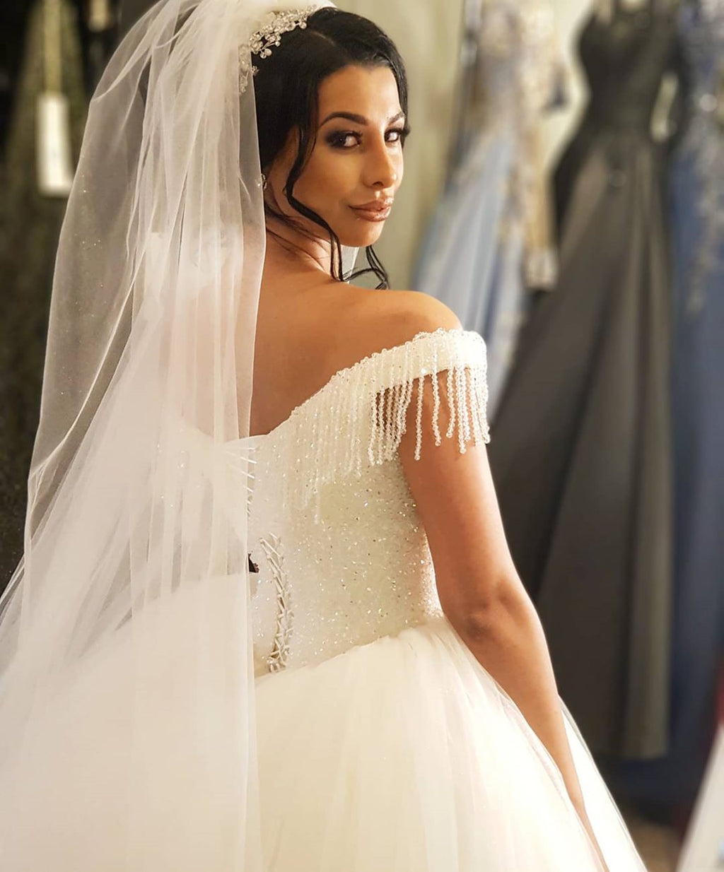 Robe de mariée longue princesse en tulle dos nu ornée de perles et de pompons, épaules dénudées, coupe princesse.