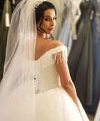 Robe de mariée longue princesse en tulle dos nu ornée de perles et de pompons, épaules dénudées, coupe princesse.