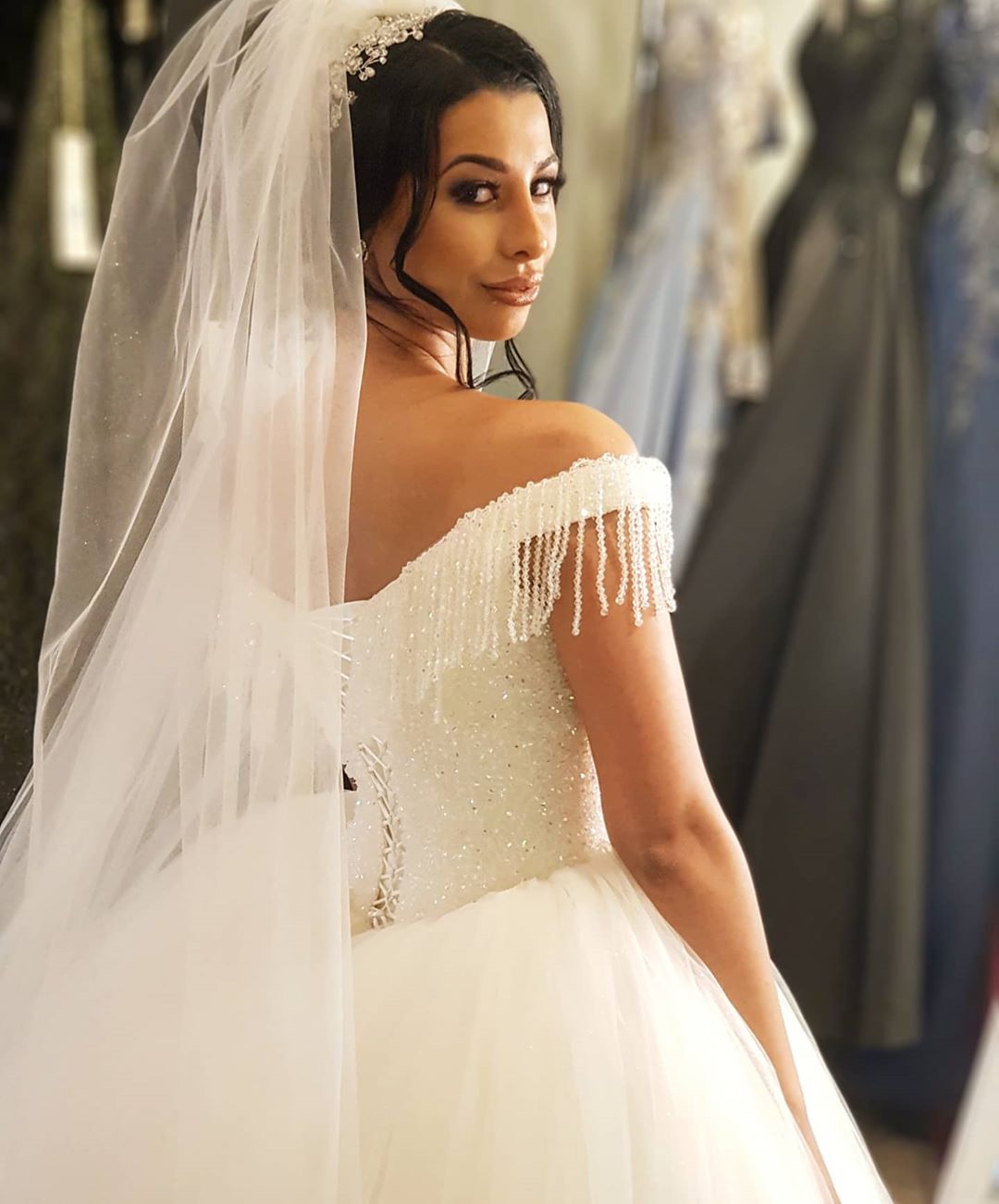 Robe de mariée longue princesse en tulle dos nu ornée de perles et de pompons, épaules dénudées, coupe princesse.