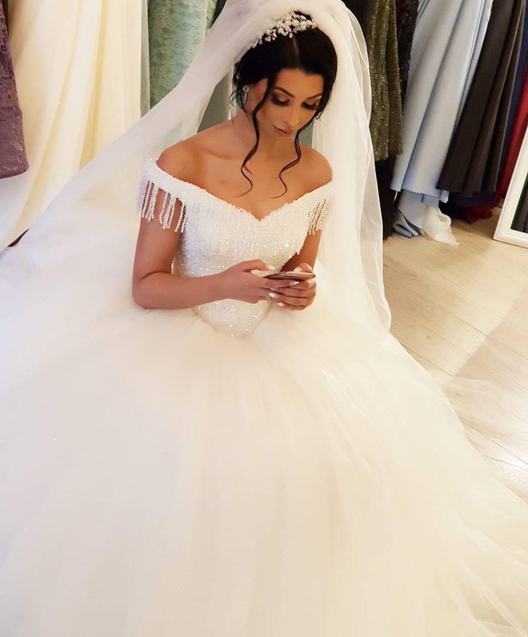 Robe de mariée longue princesse en tulle dos nu ornée de perles et de pompons, épaules dénudées, coupe princesse.