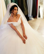 Robe de mariée longue princesse en tulle dos nu ornée de perles et de pompons, épaules dénudées, coupe princesse.