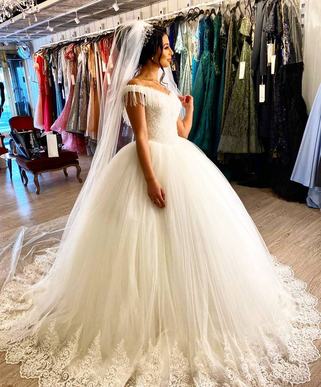 Robe de mariée longue princesse en tulle dos nu ornée de perles et de pompons, épaules dénudées, coupe princesse.