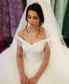 Robe de mariée longue princesse en tulle dos nu ornée de perles et de pompons, épaules dénudées, coupe princesse.