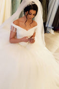 Robe de mariée longue princesse en tulle dos nu ornée de perles et de pompons, épaules dénudées, coupe princesse.