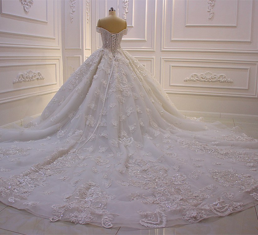 Robe de mariée longue princesse en tulle, décolleté cœur, épaules dénudées, dos nu, ornée d'appliques en dentelle et de volants.