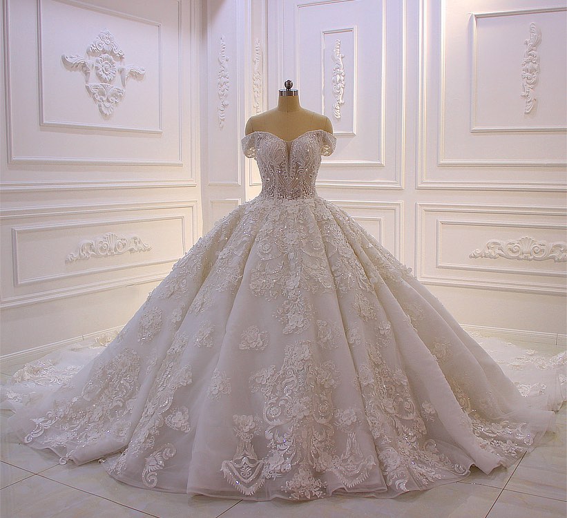 Robe de mariée longue princesse en tulle, décolleté cœur, épaules dénudées, dos nu, ornée d'appliques en dentelle et de volants.
